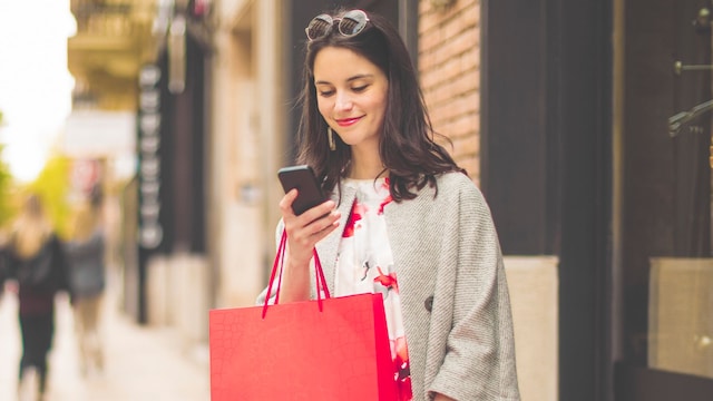 Mujer con bolsas de compras en la calle mirando su teléfono móvil