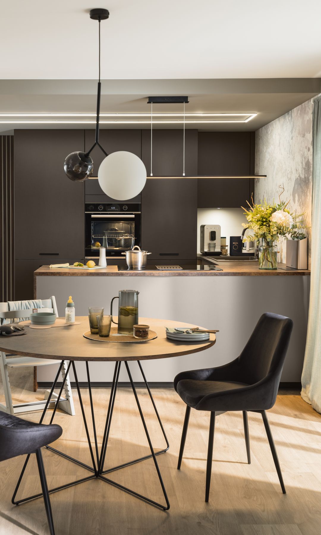Cocina con office con muebles grises, mesa de comedor redonda, sillas negras, lámpara de techo